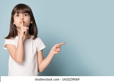 Adorable six years old little girl holding finger on lips symbol of hush gesture of asking to be quiet. Silence or secret concept image isolated on blue studio background with copy free space for text