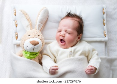 Adorable sleepy newborn baby with a toy bunny yawning in bed - Powered by Shutterstock