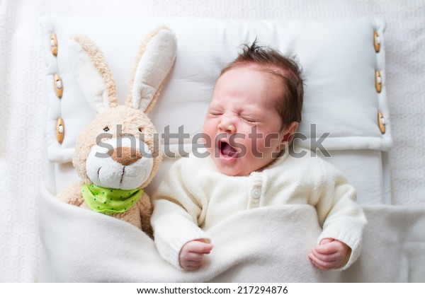 ベッドであくびをするおもちゃのバニーを持つ かわいらしい眠い新生児 の写真素材 今すぐ編集