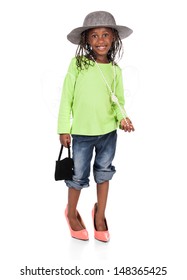 Adorable Small African Child With Braids Wearing A Bright Green Shirt And Blue Jeans. The Girl Is Playing Dress Up With A Hat And High Heels.