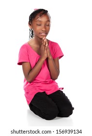 Adorable Small African Child With Braids Wearing A Bright Green Shirt And Black Skinny Jeans. The Girl Is Kneeling And Praying.