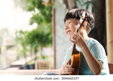 An Adorable And Smart Asian Little Boy Happy Playing Song With His Ukulele At Home. Copy Space, Early Childhood, Learning Music Instrument, Talented, Sensory, Montessori, Fine Motor Skills, Cute.