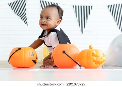 Adorable Smiling African Baby Kid Dress Up In Vampire Fancy Halloween Costume With Black Bat Wings, Cute Child Go To Party, Play Trick Or Treat, Hold Orang Pumpkin Basket. Happy Halloween Celebration