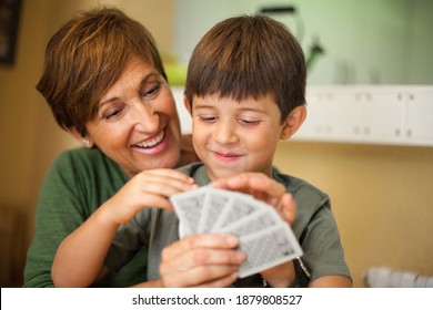 Adorable smiling couple of boy and his grandmother sitting together and smiling while they are playing a cards game. Spending quality leisure time with children and family concept.