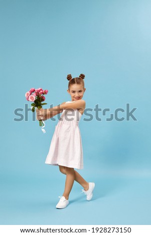 adorable smiling little girl holding bouquet of roses isolated on blue studio background. child gives bouquet to mom. mothers day