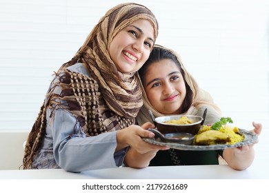 Adorable Smiling Pakistani Muslim Girl And Mother At Kitchen, Hold Tray Of Traditional Islamic Food, Daughter And Mom Wear Hijab, Show Halal Food To Camera, Happy Islamic Family On White Background. 