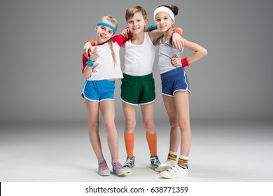 Adorable smiling sporty kids in sportswear standing together isolated on grey, children sport concept
