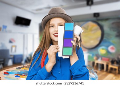 Adorable student girl wearing hat with watercolor painting and palette at art studio or classrooom