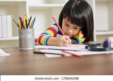 Adorable talented Asian girl sitting at desk at home and drawing with red pencil - Powered by Shutterstock