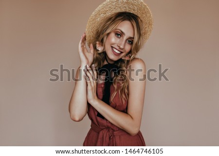 Adorable tanned girl in canotier posing on brown background. Studio shot of smiling gorgeous blonde lady in straw hat.