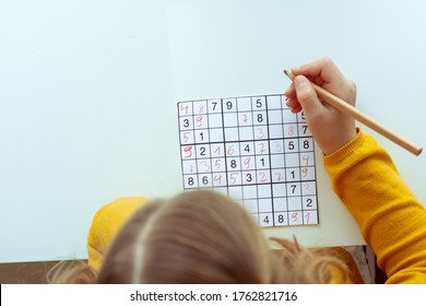 Adorable teen girl solving sudoku at desk at school or at home. View from above