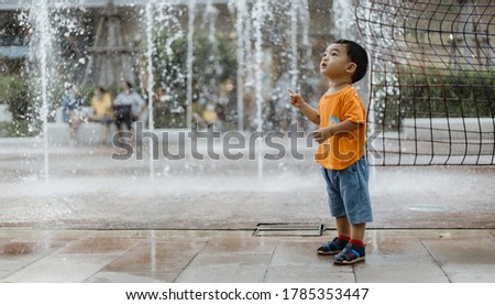 An adorable toddler Asian boy (1-year-old) standing and enjoy to see outdoor public fountains a water splashing for the first time. Thailand plays and fun space for kids. Vacation and holiday concept.