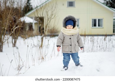 Adorable Toddler Boy Having Fun In A Backyard On Snowy Winter Day. Cute Child Wearing Warm Clothes Playing In A Snow. Winter Activities For Family With Kids.