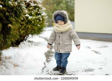 Adorable Toddler Boy Having Fun In A Backyard On Snowy Winter Day. Cute Child Wearing Warm Clothes Playing In A Snow. Winter Activities For Family With Kids.