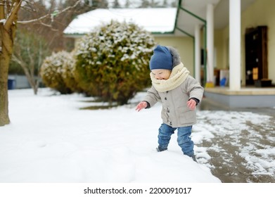 Adorable Toddler Boy Having Fun In A Backyard On Snowy Winter Day. Cute Child Wearing Warm Clothes Playing In A Snow. Winter Activities For Family With Kids.