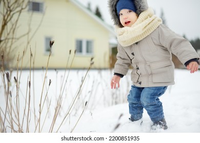 Adorable Toddler Boy Having Fun In A Backyard On Snowy Winter Day. Cute Child Wearing Warm Clothes Playing In A Snow. Winter Activities For Family With Kids.