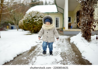 Adorable Toddler Boy Having Fun In A Backyard On Snowy Winter Day. Cute Child Wearing Warm Clothes Playing In A Snow. Winter Activities For Family With Kids.