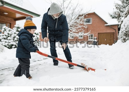 Adorable toddler boy helping his grandfather to shovel snow in a backyard on winter day. Cute child wearing warm clothes playing in a snow. Winter activities for family with kids.