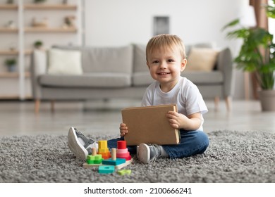 Adorable toddler boy holding book while playing with stacking and sorting toy at home, sitting on carpet and smiling at camera, having fun, kid and study, education concept - Powered by Shutterstock