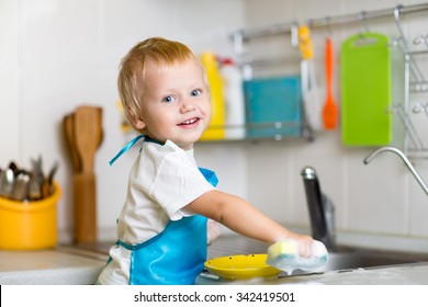 Adorable Toddler Child Washing Dishes In Kitchen. Little Boy Having Fun With Helping To His Mother With Housework.