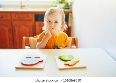 Adorable Toddler Girl Doing Wooden Puzzle, Looking Confused, Not Sure What To Do Next. Kid Learning To Solve Problems And Developing Cognitive Skills