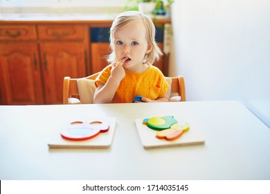 Adorable Toddler Girl Doing Wooden Puzzle, Looking Confused, Not Sure What To Do Next. Kid Learning To Solve Problems And Developing Cognitive Skills