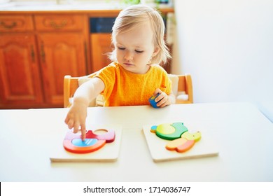 Adorable Toddler Girl Doing Wooden Puzzle, Looking Confused, Not Sure What To Do Next. Kid Learning To Solve Problems And Developing Cognitive Skills