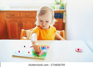 Adorable toddler girl doing wooden puzzle. Child learning geometric shapes. Kid learning to solve problems and developing cognitive skills