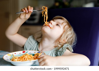 Adorable toddler girl eat pasta spaghetti with tomato bolognese with minced meat. Happy preschool child eating fresh cooked healthy meal with noodles and vegetables at home, indoors.
