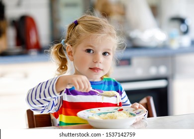 Adorable Toddler Girl Eating Healthy Chicken Noodle Soup For Lunch. Cute Happy Baby Child Taking Food At Home Or Nursery Daycare Or Kindergarten And Learning Using Spoon.