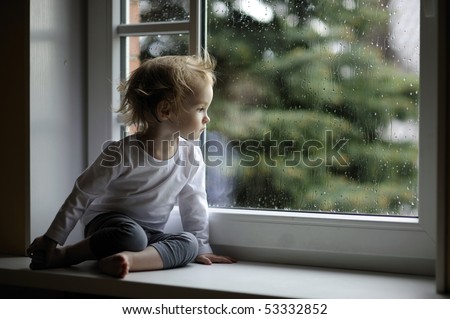 Adorable toddler girl looking at raindrops on the window