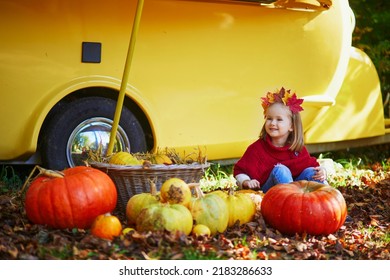 Adorable Toddler Girl In Maple Leaves Wreath Sitting On The Ground Near Many Pumpkins. Happy Kid Celebrating Halloween