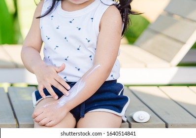 Adorable Toddler Girl Putting Solar Cream On Arms Hands Smiling Happy Outdoors By Pool Under Sunshine On Beautiful Summer Day.Mixed Race Asian / Caucasian Kid Girl.Sunscreen Or Sunblock And Skincare.