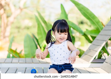 Adorable Toddler Girl Putting Solar Cream On Arms Hands Smiling Happy Outdoors By Pool Under Sunshine On Beautiful Summer Day.Mixed Race Asian / Caucasian Kid Girl.Sunscreen Or Sunblock And Skincare.