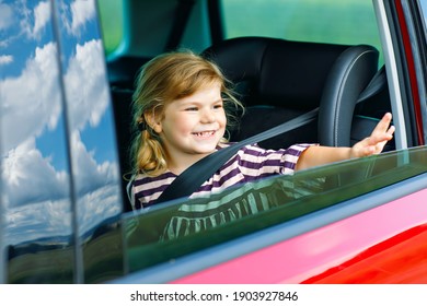 Adorable Toddler Girl Sitting In Car Seat And Looking Out Of The Window On Nature And Traffic. Little Kid Traveling By Car. Child Safety On The Road. Family Trip And Vacations In Summer