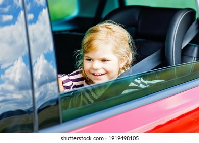 Adorable Toddler Girl Sitting In Car Seat And Looking Out Of The Window On Nature And Traffic. Little Kid Traveling By Car. Child Safety On The Road. Family Trip And Vacations In Summer