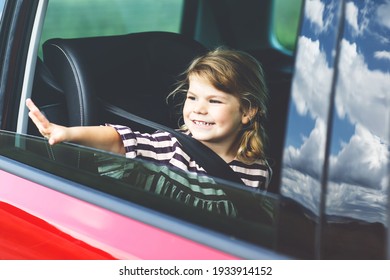 Adorable Toddler Girl Sitting In Car Seat And Looking Out Of The Window On Nature And Traffic. Little Kid Traveling By Car. Child Safety On The Road. Family Trip And Vacations In Summer