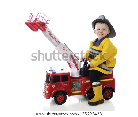 An adorable toddler happily playing fireman on his toy fire truck.  On a white background.