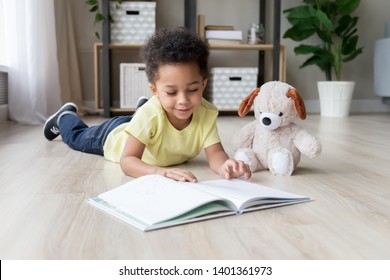 Adorable Toddler Mixed Race Boy Reading Book At Home Or In Kindergarten, Beautiful Preschooler Child With Toy Lying On Warm Floor, Playing, Having Fun, Kid And Study, Education Concept