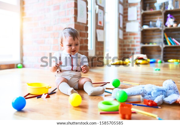 Adorable toddler playing around lots of toys\
and crying at\
kindergarten