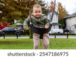 Adorable toddler smiling while swinging at a park surrounded by autumn colors. Captured in a cozy neighborhood, reflecting joy and playfulness on a crisp fall day.