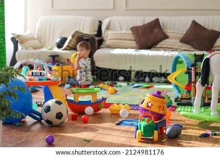 Adorable toddlers playing among the many toys at home. A mess in the children's room, a lot of toys in the children's room. Dirty house. Children's room
