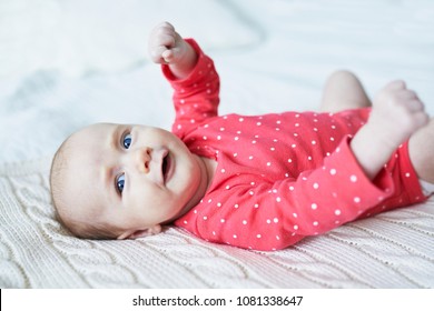 Adorable two months baby girl relaxing in bedroom on knitted blanket on a sunny morning