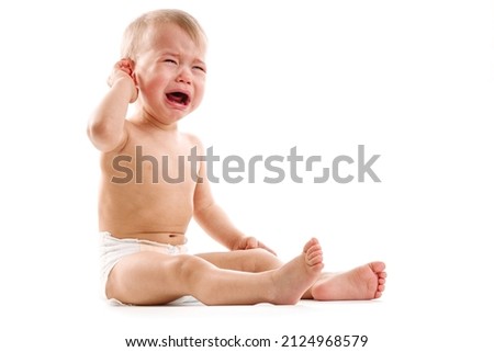 Adorable upset little boy in diaper is sitting and crying on white background.