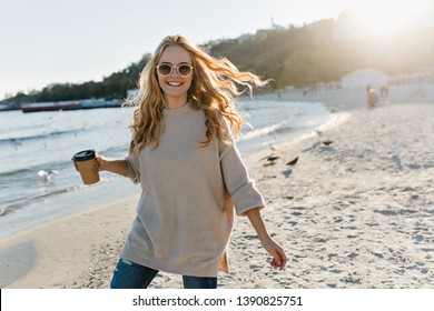 Adorable woman in casual sweater posing at sea. Stunning fair-haired girl enjoying autumn day near ocean - Powered by Shutterstock