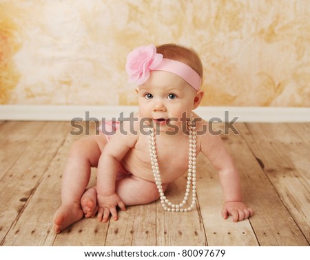 Adorable young baby girl wearing a vintage pearl necklace and pink rose headband