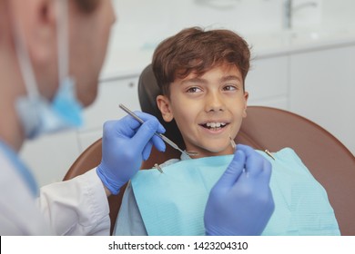 Adorable young boy visiting dentist, having his teeth checked by dentist. Lovely happy kid smiling with healthy teeth, getting his dental examination