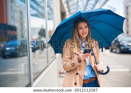 Adorable young business woman with a seductive look, standing in the street, holding umbrella and phone