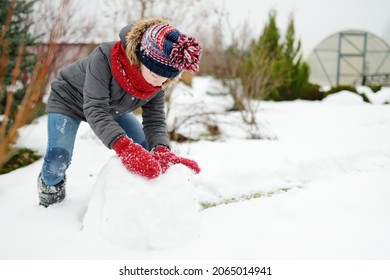 Adorable Young Girl Building A Snowman In The Backyard. Cute Child Playing In A Snow. Winter Activities For Family With Kids.