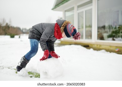 Adorable Young Girl Building A Snowman In The Backyard. Cute Child Playing In A Snow. Winter Activities For Family With Kids.